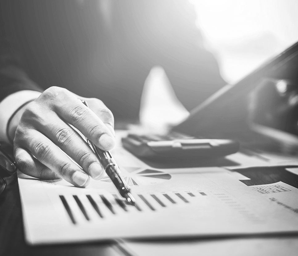 Hand holding a pen gesturing at a paper with column graphs and pie charts