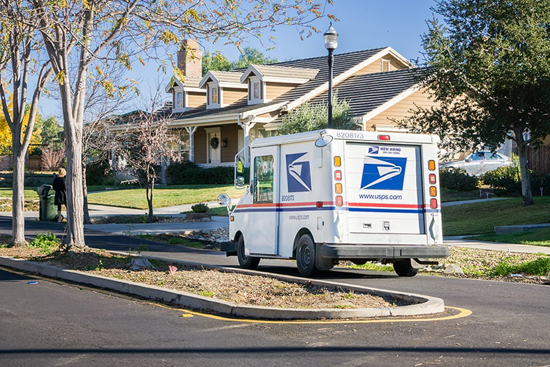 USPS mail truck on a residential street in front of a home.