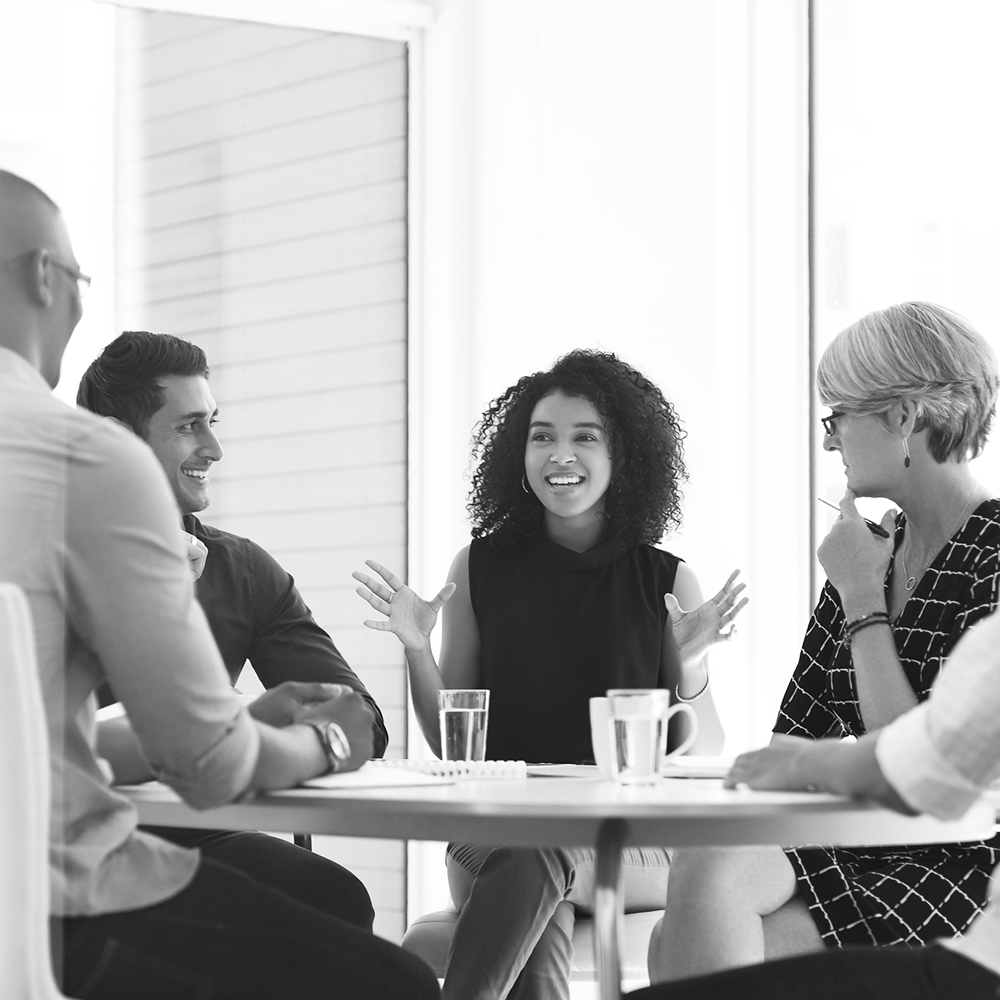 A group of five people seated around a round table with glasses and mugs placed in front of them as well as papers