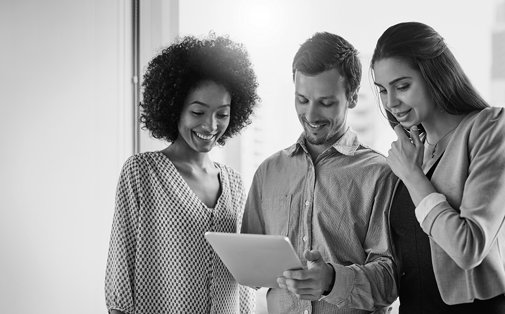 black and white image of three people gathered around a tablet screen